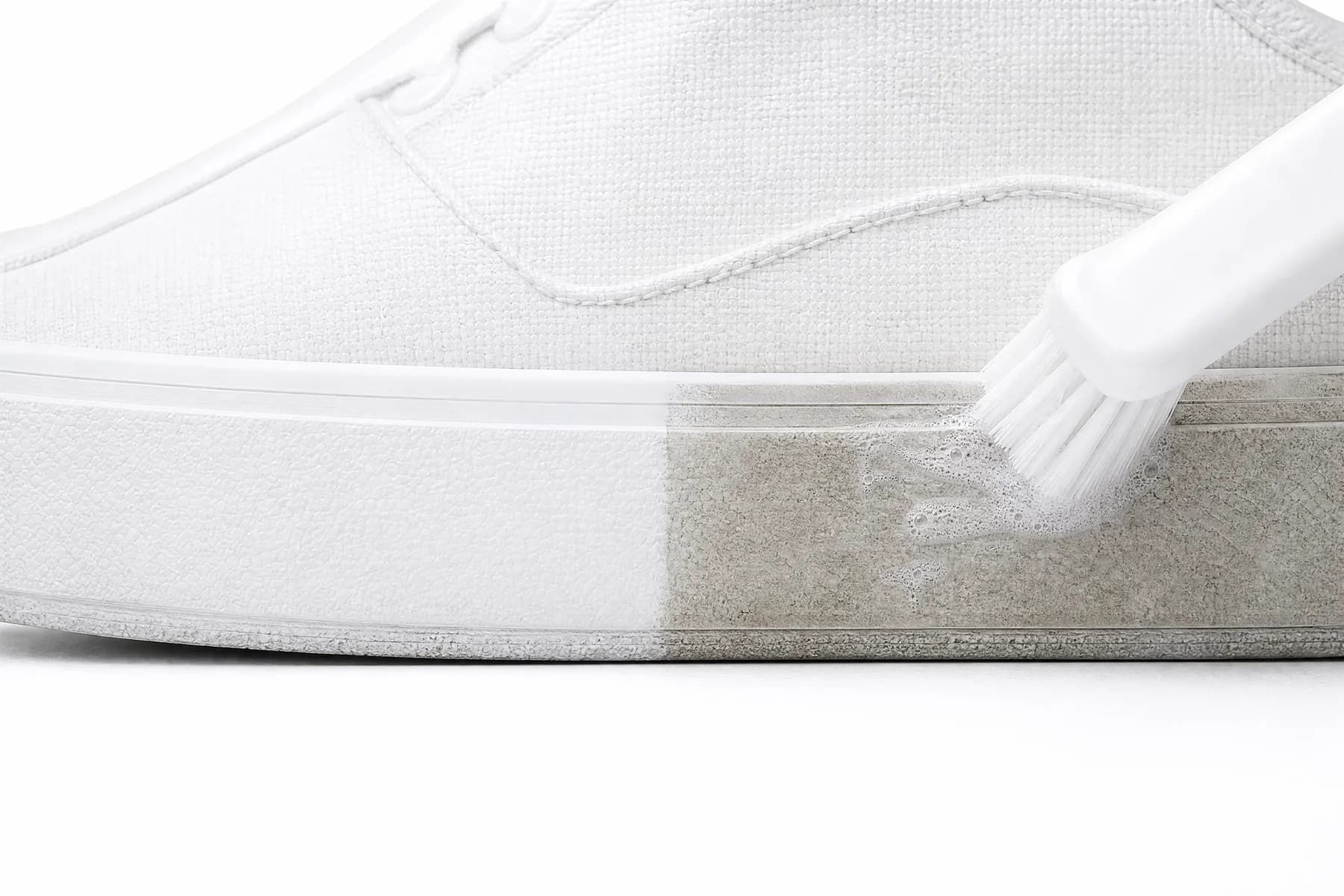 A white rubber midsole being scrubbed with a stiff brush, half clean and half still grey